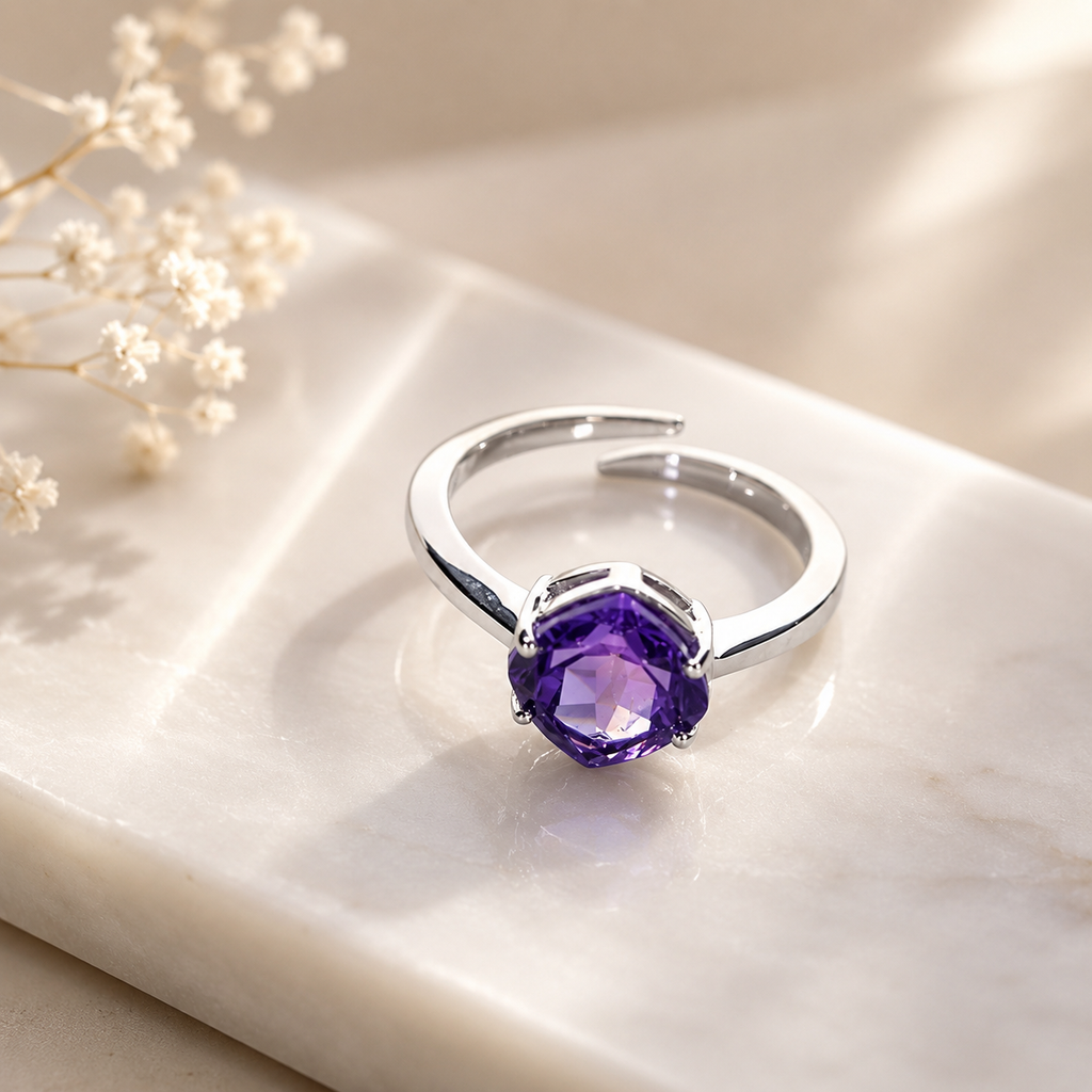 Silver ring with a purple gemstone on a light surface with dried flowers.