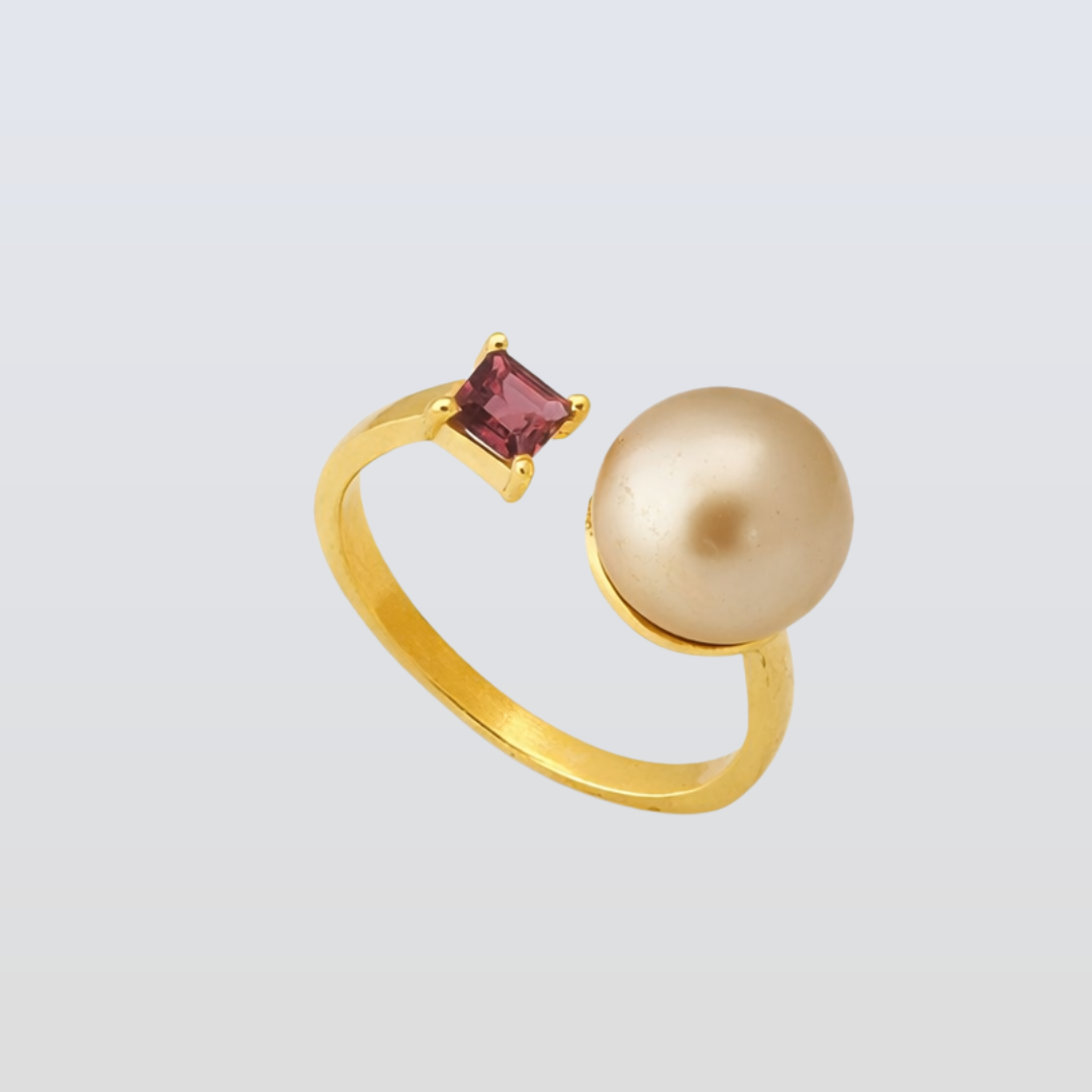 Gold ring with a pearl and a red gemstone on a light gray background