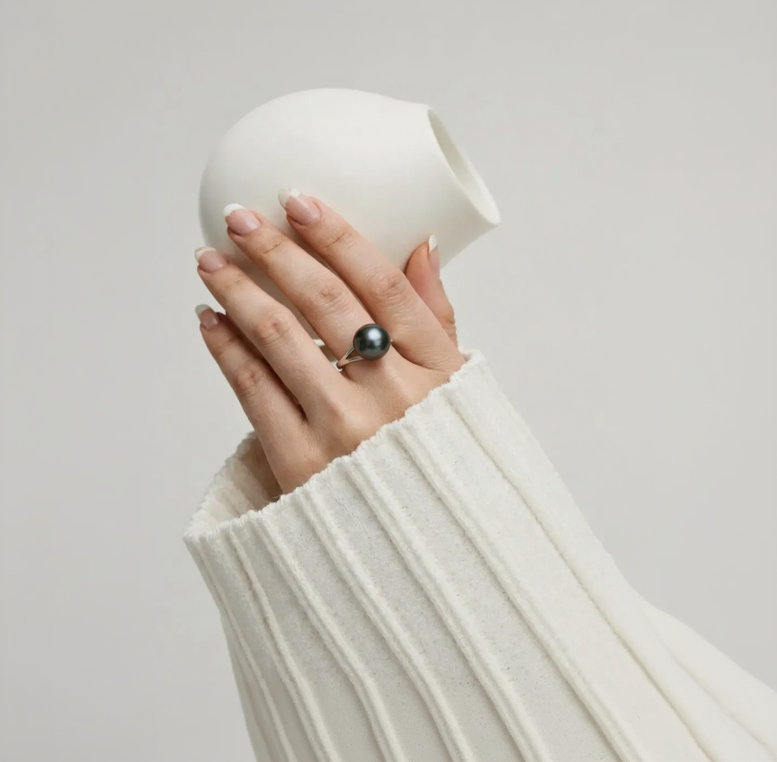 Hand wearing a black pearl ring with a white ceramic cup in the background