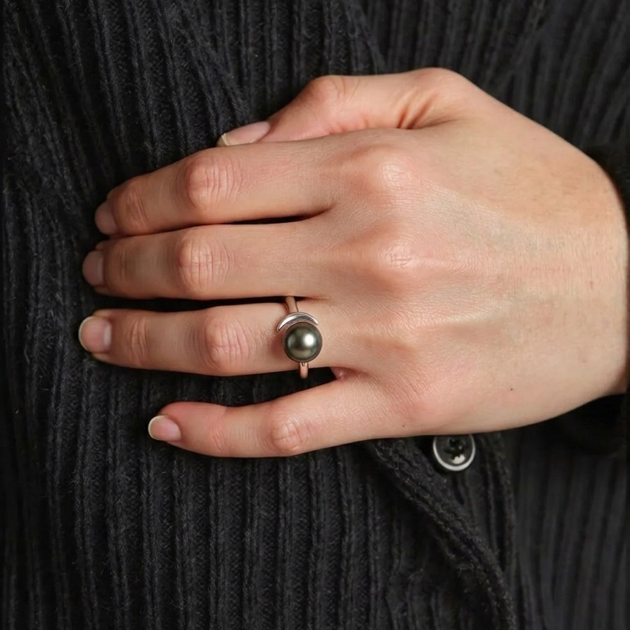 Hand wearing a ring with a pearl on a dark textured fabric background