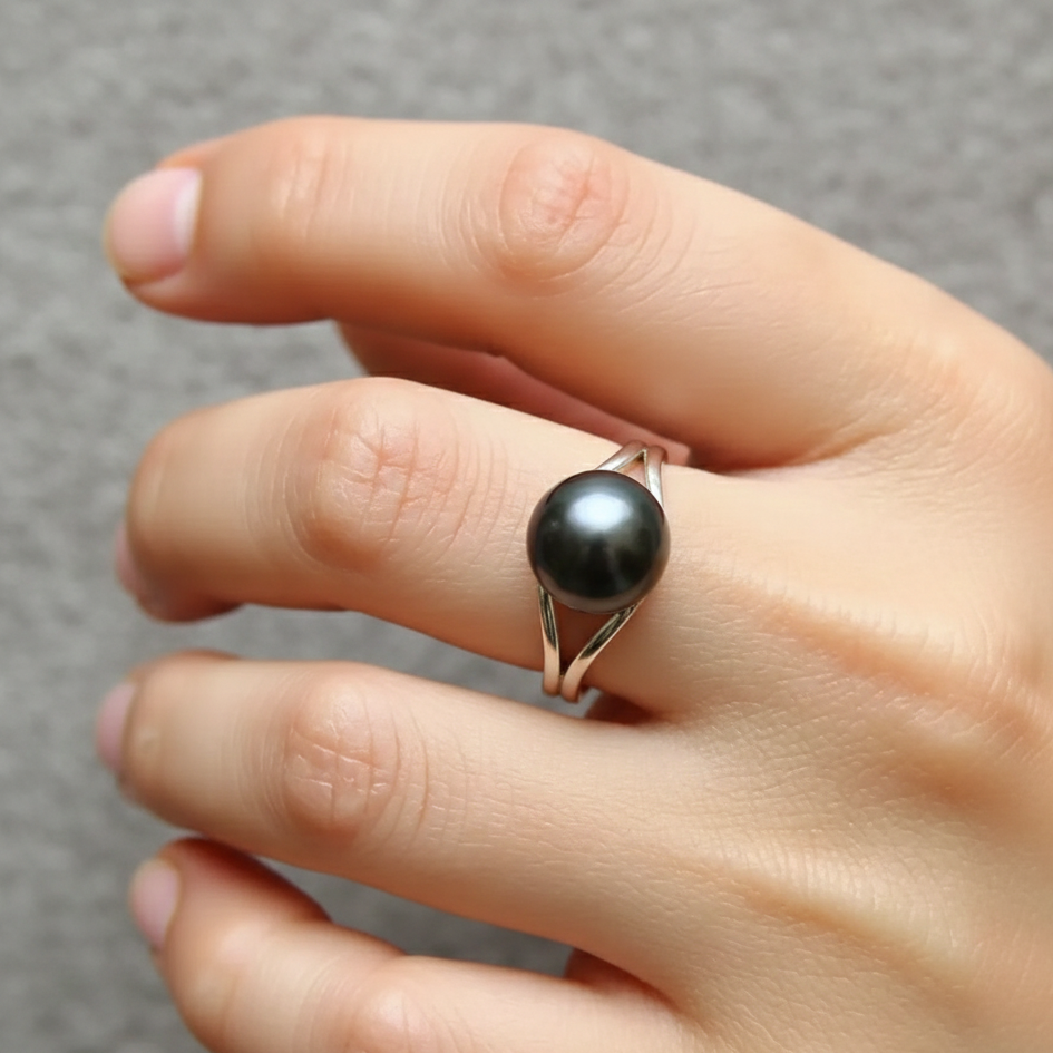 Hand wearing a black pearl ring on a gray background