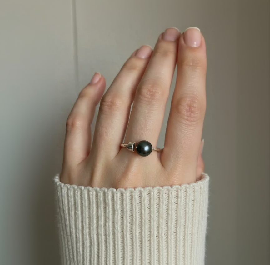 Hand wearing a ring with a black pearl on a neutral background