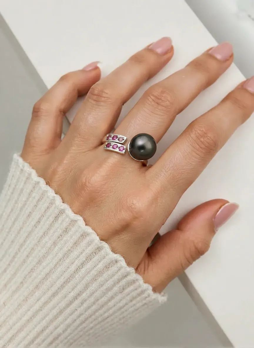 Hand wearing a ring with a black gemstone and pink stones on a light background