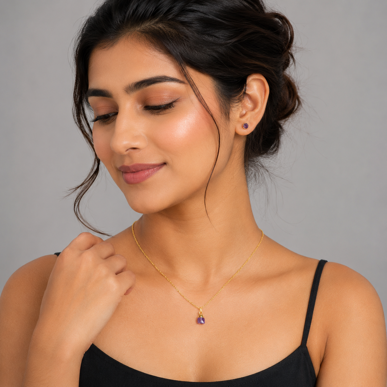 Woman wearing a gold necklace with a pendant against a gray background