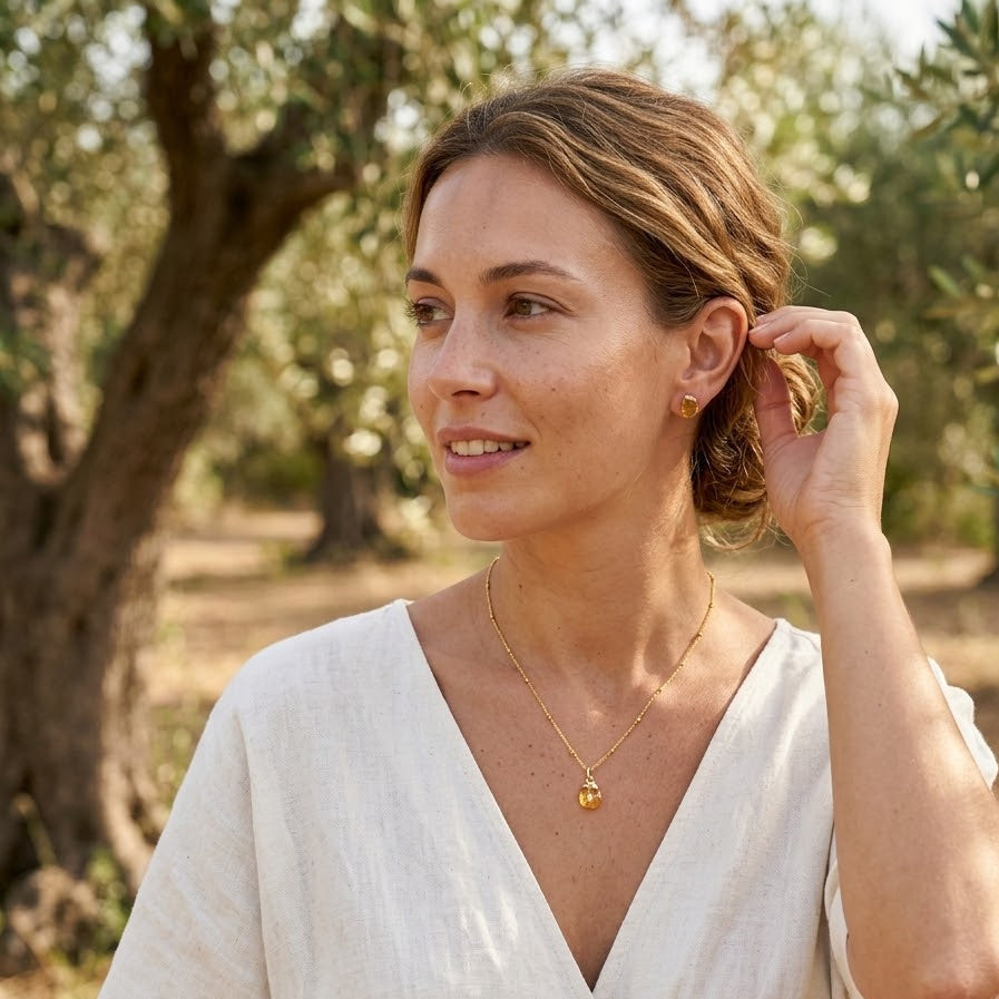 Woman in a white dress standing wearing gemstone jewellery set in an olive grove