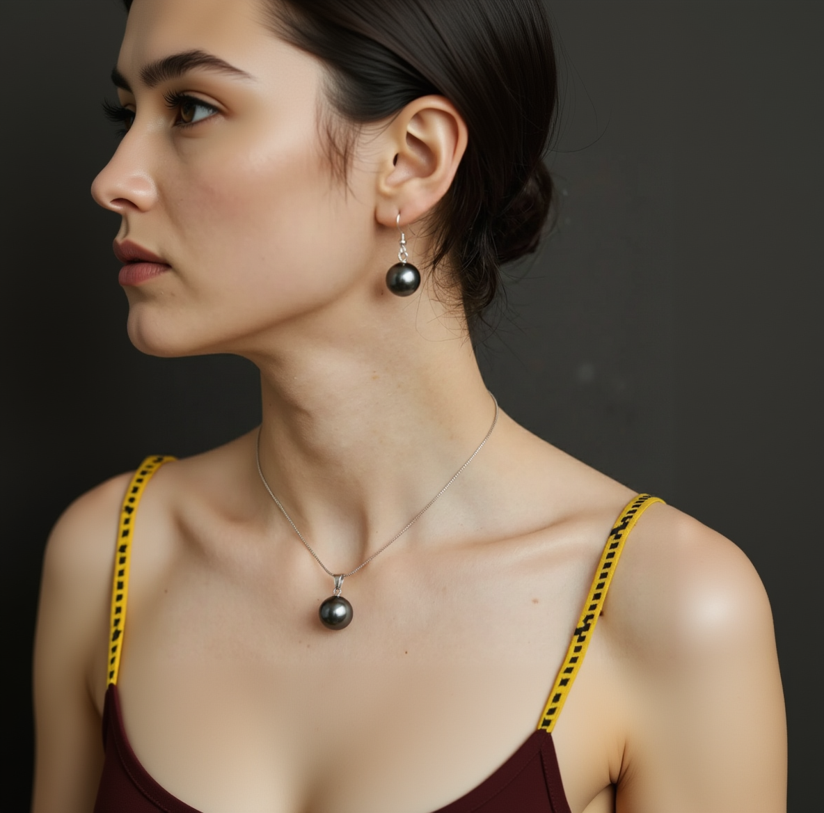 Close-up of a woman wearing black pearl earrings and necklace against a dark background