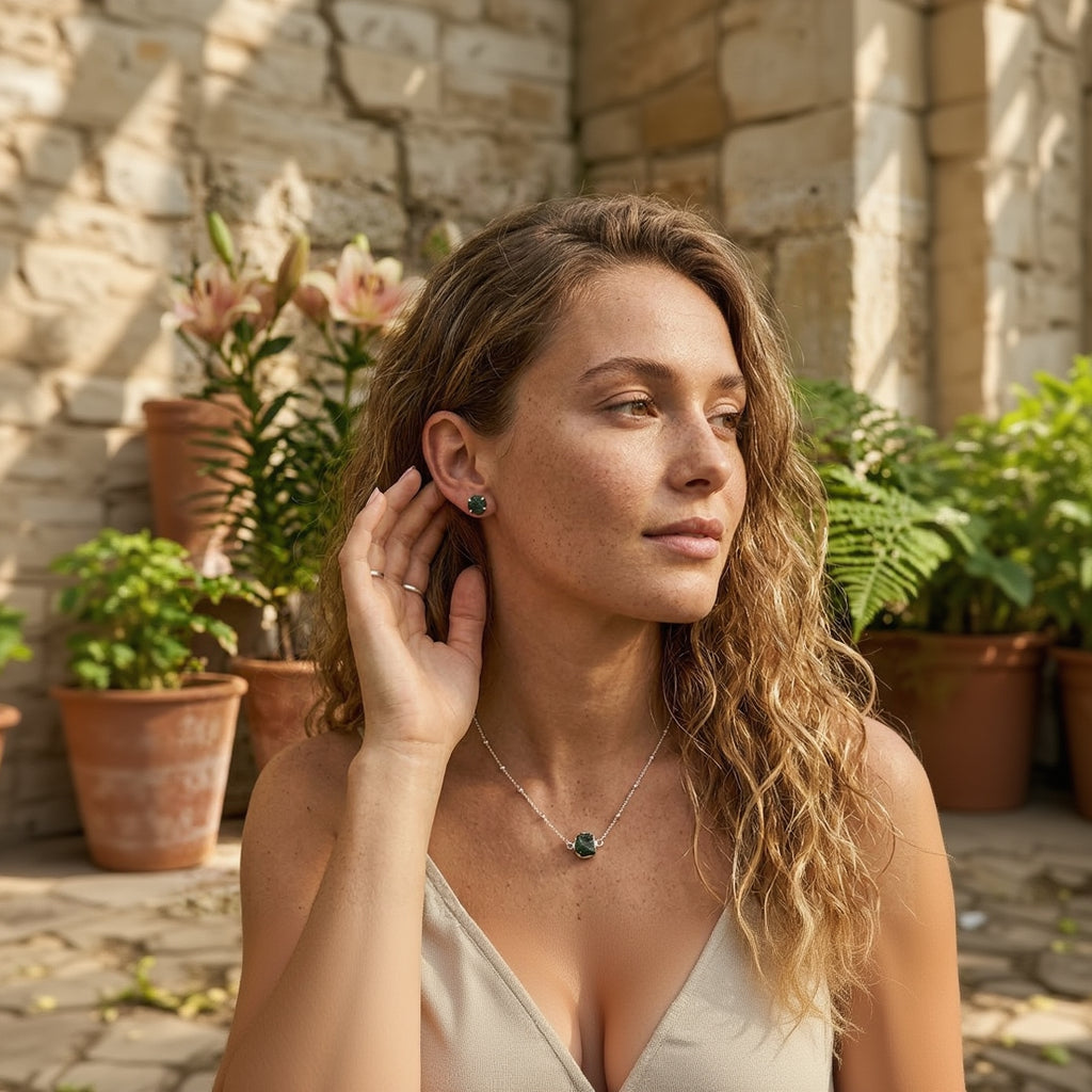 Woman adjusting an earring outdoors with plants in the background