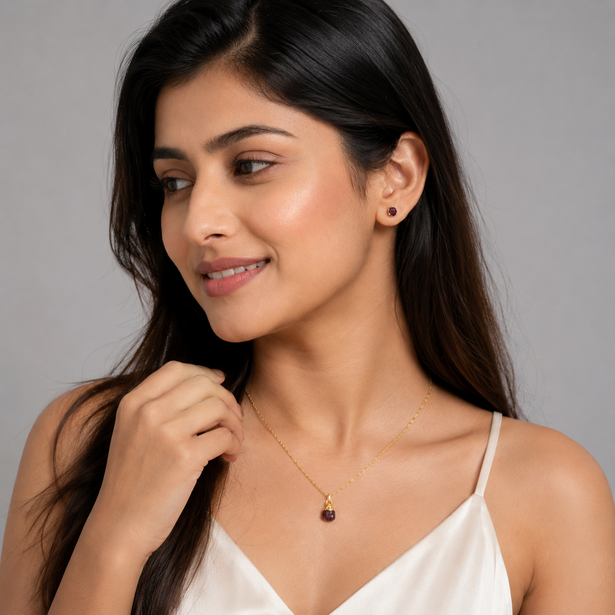 Woman wearing a gold necklace with a red gemstone on a gray background