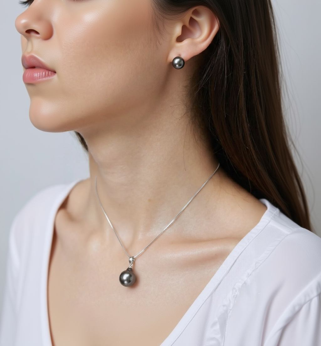 Close-up of a person wearing a silver necklace with a pendant and black earrings.