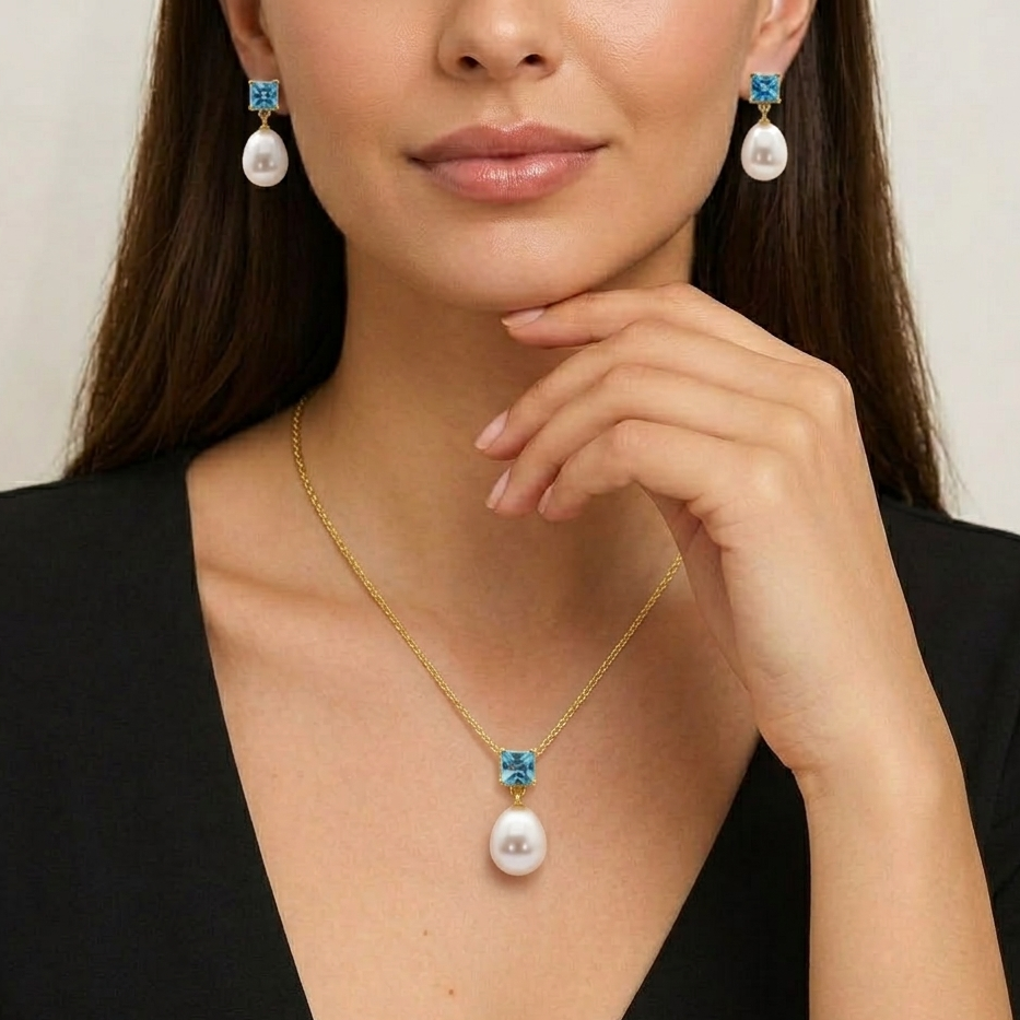 Woman wearing a gold necklace with pearl and blue gemstone pendant and matching earrings.