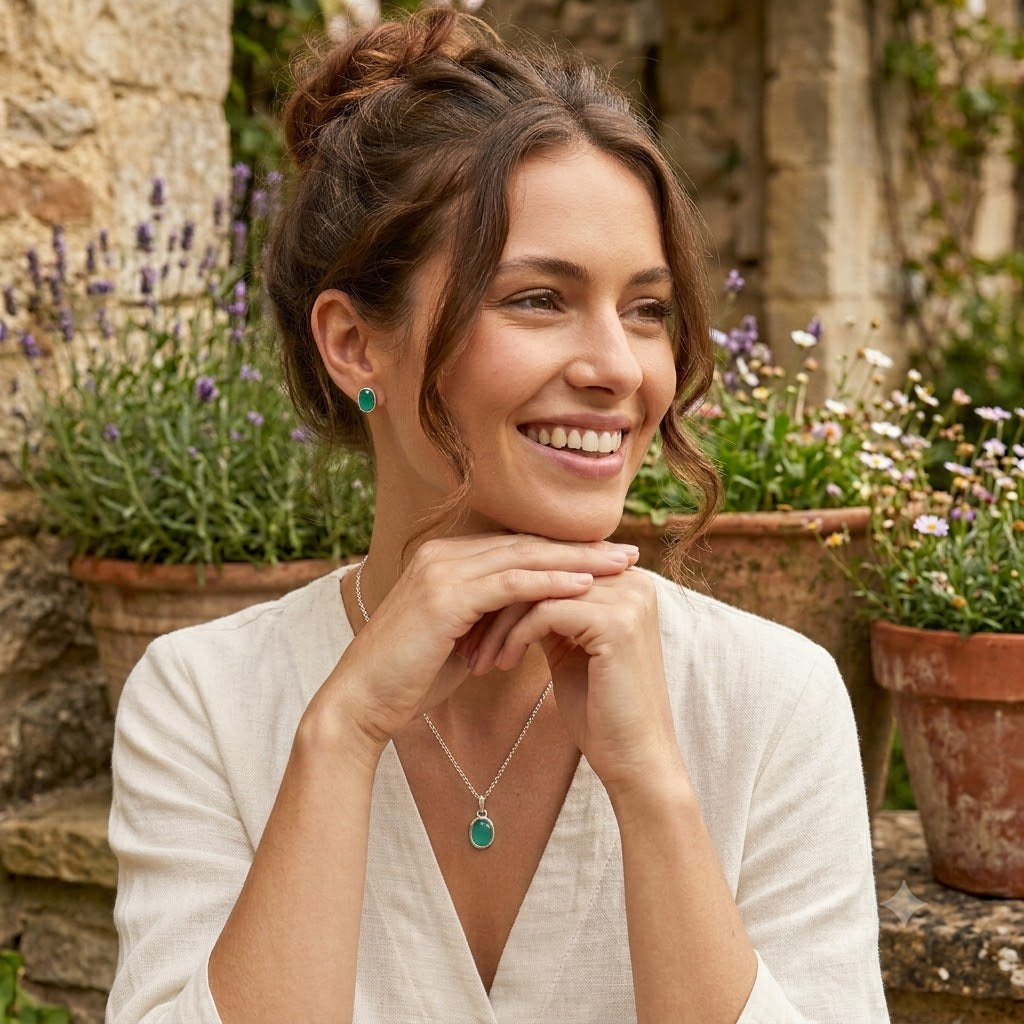 Woman wearing green earrings and a necklace, standing in a garden with potted plants.