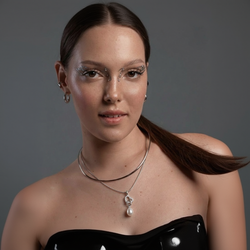 Woman wearing a necklace with a pearl pendant against a gray background