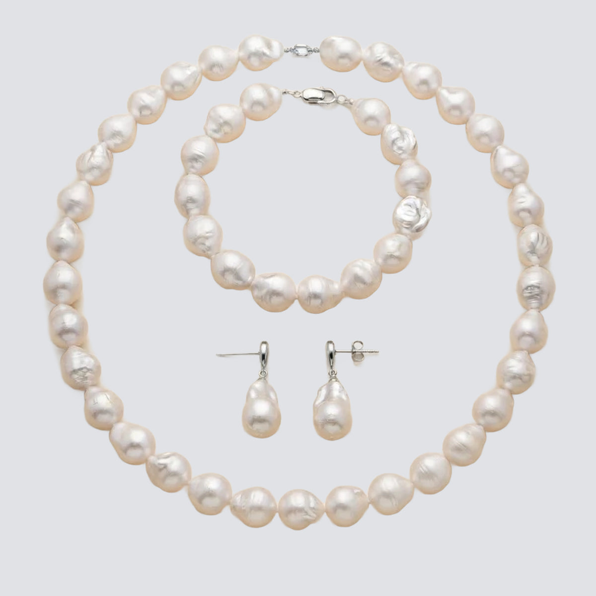 A pearl jewelry set on a light gray background, including a strand necklace, a bracelet, and a pair of drop earrings in silver-tone metal.