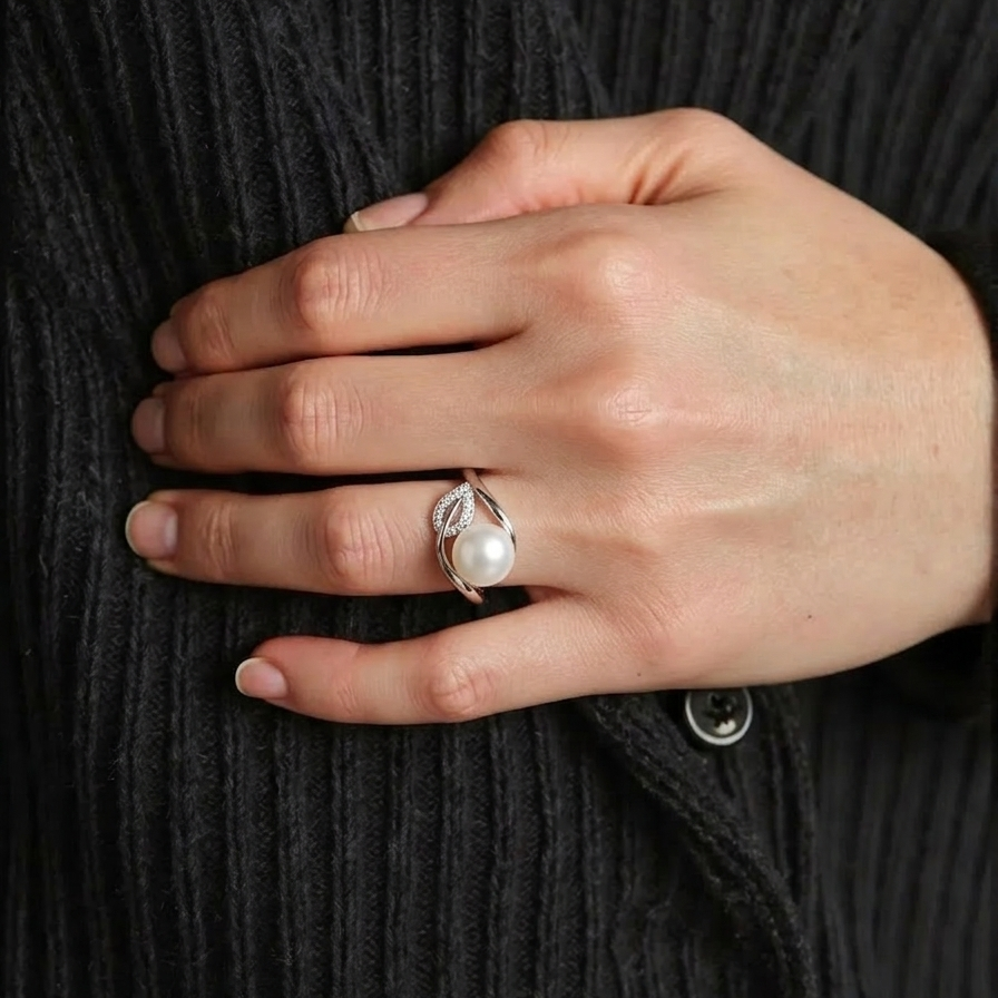 Hand wearing a ring with a pearl on a dark textured background